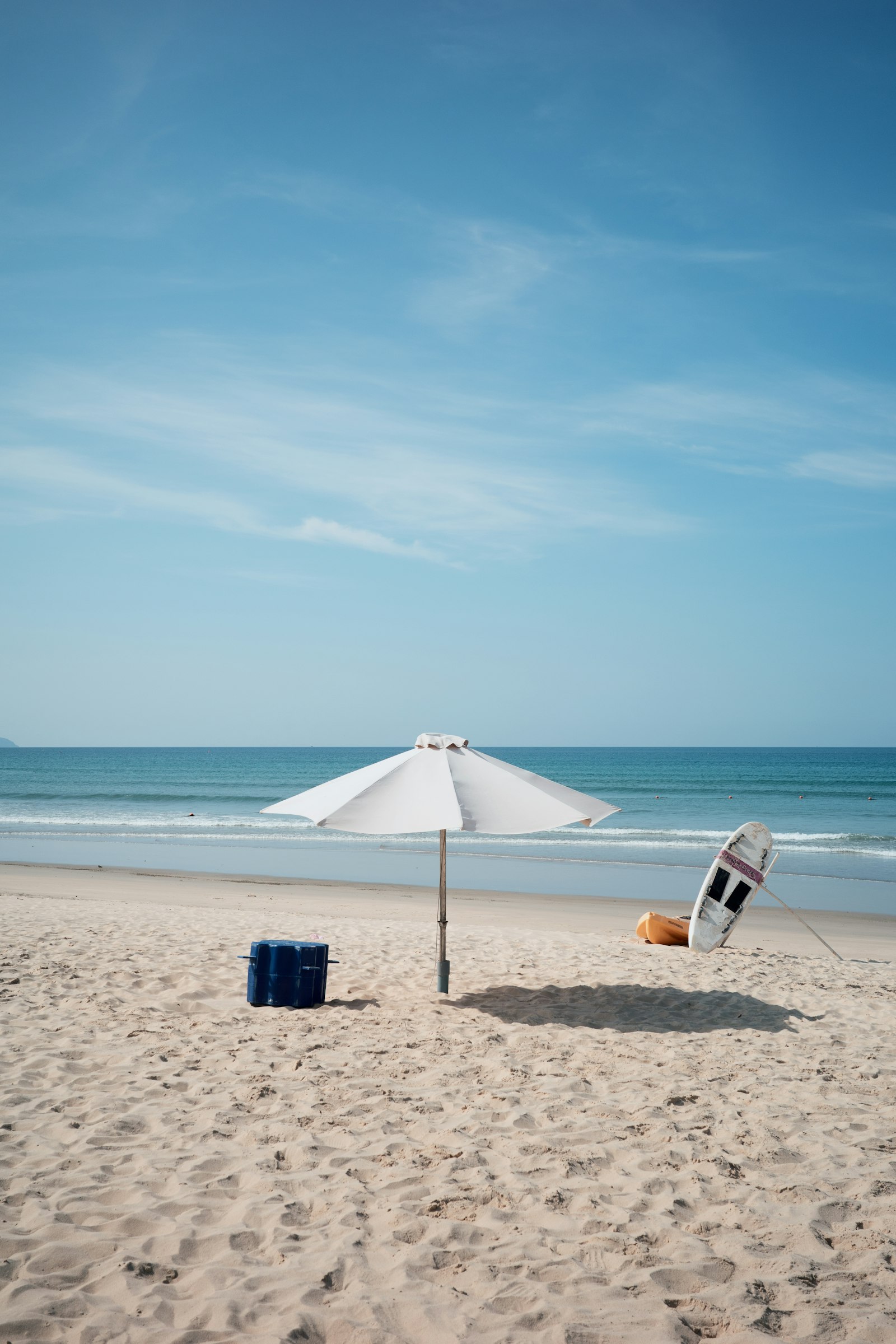 A cooler, umbrella, and surfboard on a sunny beach